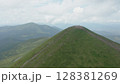 Aerial view of the approaching mountain peak against the backdrop of a beautiful mountain landscape and cloudy blue sky. Many travelers can be seen at the top of the mountain. 128381269
