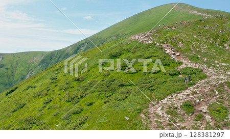 Aerial view of young tourists walking along a mountain trail with backpacks to the top of the mountain. Hiking, climbing, traveling, trekking, backpacking. Aerial view of young tourists walking along a mountain trail with backpacks to the top of the mountain. Hiking, climbing, traveling, trekking, backpacking. 128381297