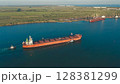 Aerial view of a large cargo ship leaving the harbor with tugboats at sunset. On the horizon in the roadstead there are ships waiting for the entrance to the port. 128381299
