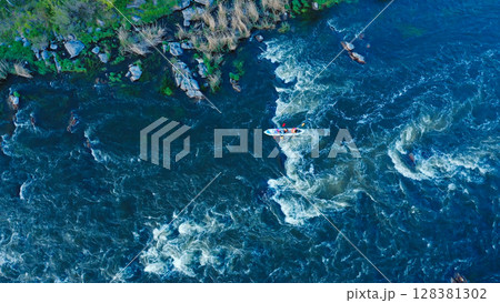 Aerial view of a kayak boat rushing along with a stormy stream between the stones at high speed. Rowers trying to steer the boat in the right direction. Aerial view of a kayak boat rushing along with a stormy stream between the stones at high speed. Rowers trying to steer the boat in the right direction. 128381302
