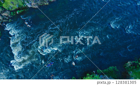 Aerial view of a kayak boat rushing along a turbulent river between stone rocks at high speed. Athletes trying to steer the boat in the right direction. Aerial view of a kayak boat rushing along a turbulent river between stone rocks at high speed. Athletes trying to steer the boat in the right direction. 128381305