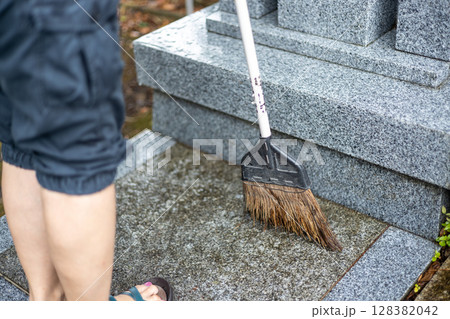 ほうきでお墓の周りを掃除している女性 128382042