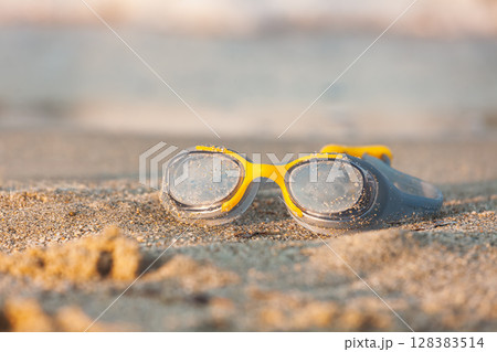 Swimming goggles on beach sand in golden sunset light Swimming goggles on beach sand in golden sunset light 128383514