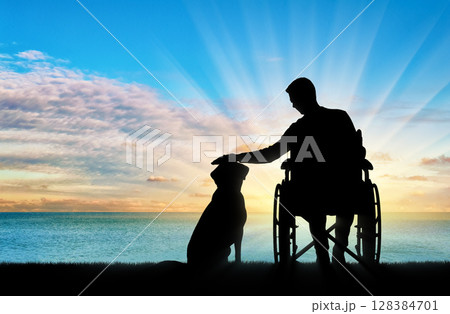 Silhouette of a disabled man in a wheelchair stroking his dog 128384701