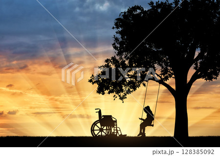Girl schoolgirl invalid sitting on a swing under a tree, reading a book, beside a wheelchair 128385092
