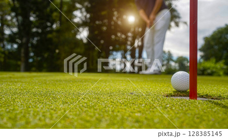 Golfer putting ball on the green golf, lens flare on sun set evening time. Golfer putting ball on the green golf, lens flare on sun set evening time. 128385145