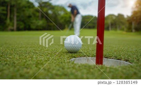 Golfer putting ball on the green golf, lens flare on sun set evening time. Golfer hitting golf ball. 128385149