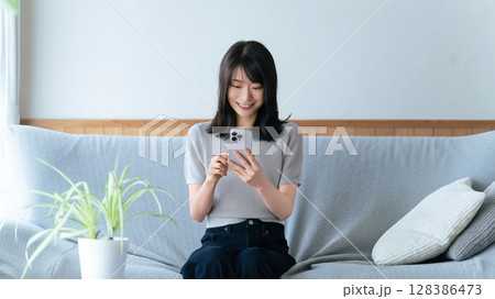 ソファに座ってスマートフォンを使う笑顔の女性 ソファに座ってスマートフォンを使う笑顔の女性 128386473