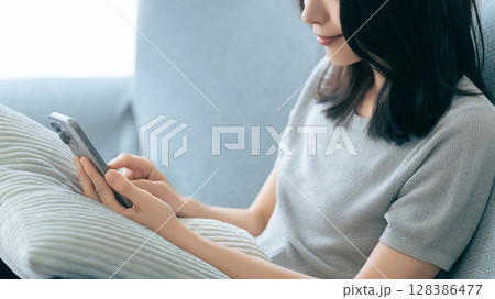 ソファに座ってスマートフォンを使う笑顔の女性 128386477