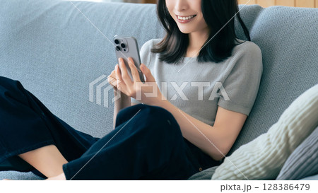 ソファに座ってスマートフォンを使う笑顔の女性 128386479