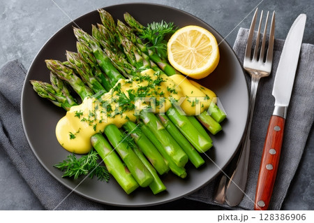 Delicious cooked asparagus with hollandaise sauce, lemon, and dill served on black plate 128386906