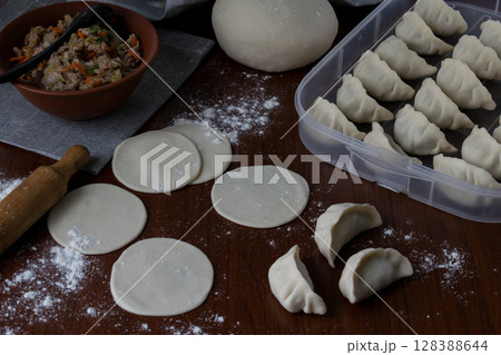 Raw dough rounds on wooden table with flour and rolling pin before filling for homemade pork gyoza preparation process traditional Japanese dumplings making step kitchen view food concept 128388644