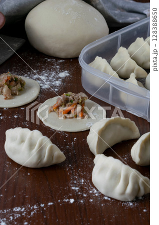 Close up view of traditional Japanese gyoza with pork filling being folded on floured board raw dough pieces and filling spoon with visible ingredients in home kitchen setting Close up view of traditional Japanese gyoza with pork filling being folded on floured board raw dough pieces and filling spoon with visible ingredients in home kitchen setting 128388650