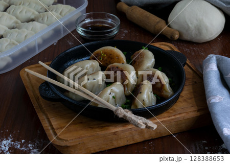 Cooked gyoza dumplings with pork filling served on cast iron pan with dipping sauce wooden tray napkin traditional Japanese dish hot meal top view close up with chopsticks 128388653
