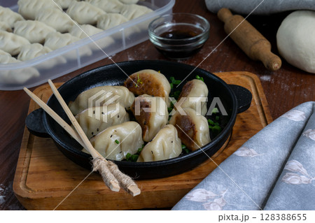 Delicious pork gyoza dumplings served in iron pan on wooden tray with chopsticks and dipping sauce close up of traditional Japanese fried dumplings meal ready to eat view Delicious pork gyoza dumplings served in iron pan on wooden tray with chopsticks and dipping sauce close up of traditional Japanese fried dumplings meal ready to eat view 128388655