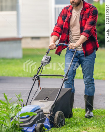Garden care. Electric lawn mower. Landscape design. Lawn mower landscaping. Backyard grass maintenance. Gardener mowing the lawn. Lawnmower mow green grass. Man gardener cut the grass 128389514