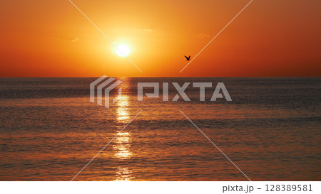 Vivid sunset over the sea with a glowing sun and golden reflection on the calm water. Peaceful and captivating atmosphere. Nature background, relaxation concept, travel theme and inspirational visual 128389581