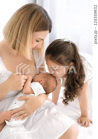 A mother breastfeeds a newborn baby. A little sister kisses her brother on the forehead while he eats. The benefits of breastfeeding A mother breastfeeds a newborn baby. A little sister kisses her brother on the forehead while he eats. The benefits of breastfeeding 128389632