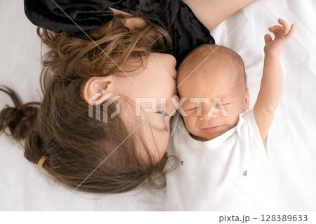 A little sister kisses a little newborn brother waking up from dream on cheek 128389633