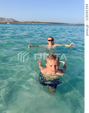 Woman and child happily swim in the clear blue ocean, enjoying a sunny day at the beach. The scene captures the joy and relaxation of a summer vacation by the seaside. Woman and child happily swim in the clear blue ocean, enjoying a sunny day at the beach. The scene captures the joy and relaxation of a summer vacation by the seaside. 128391394