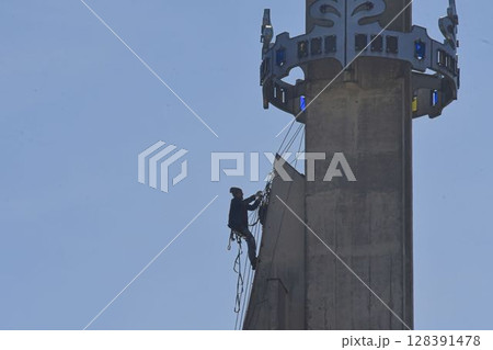 A skilled worker fixes the tower of a modern church. A roofer works on the tower of a modern building. The concept of working at height and safety at work A skilled worker fixes the tower of a modern church. A roofer works on the tower of a modern building. The concept of working at height and safety at work 128391478