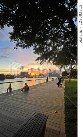 Silhouette of people, park, building, boats on bay water at sunset Silhouette of people, park, building, boats on bay water at sunset 128392218