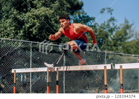 A man with a prosthetic leg is jumping over a hurdle 128394374