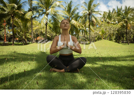Woman sits cross-legged on grass practicing mindfulness in nature 128395830