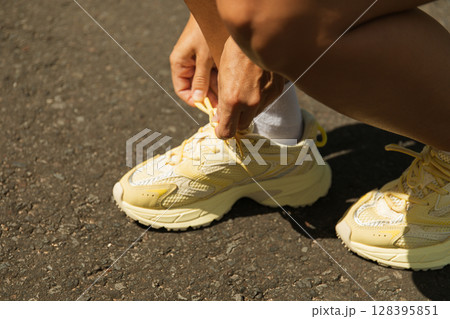 A person ties bright yellow sneakers by the pavement A person ties bright yellow sneakers by the pavement 128395851