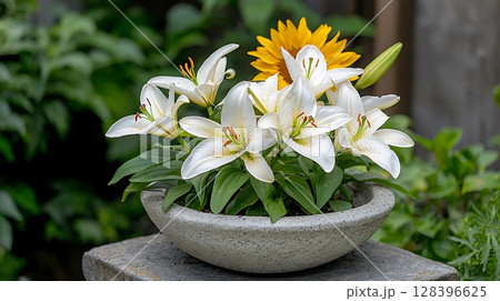 Fresh white lilies and bright sunflower arranged in a decorative stone bowl with greenery 128396625