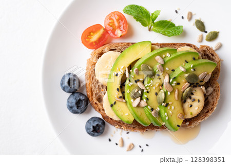 Avocado toast with banana, sunflower seeds, pumpkin seeds, sesame seeds, blueberry, tomato and honey 128398351