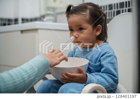 mother making nasal wash for toddler girl with syringe and saline. cleaning nose 128401197