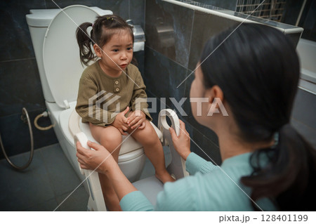 mother is helping toddler girl use the toilet. potty training and learning in bathroom 128401199