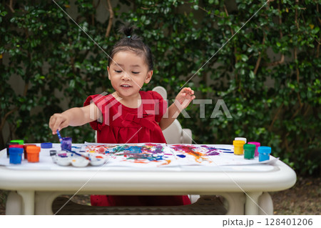 happy toddler girl painting watercolor in paper at backyard. happy toddler girl painting watercolor in paper at backyard. 128401206