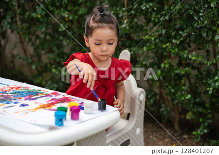 happy toddler girl painting watercolor in paper at backyard. 128401207