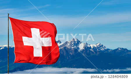 Swiss flag waving against a backdrop of majestic mountains on a clear day in the Swiss Alps Swiss flag waving against a backdrop of majestic mountains on a clear day in the Swiss Alps 128404809