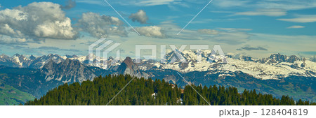 Majestic mountain landscape with snow-capped peaks and lush greenery under a clear blue sky 128404819