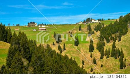 Scenic view of green hills and wooden cabins under a clear blue sky in a mountainous area during daytime 128404821
