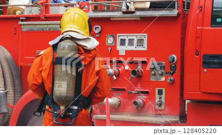 Fireman prepare equipment fighting extinguisher at fire engine truck. Firefighter fighting with smoke flame using fire hose, tube, chemical water foam spray at truck. Fireman wear hard hat protection Fireman prepare equipment fighting extinguisher at fire engine truck. Firefighter fighting with smoke flame using fire hose, tube, chemical water foam spray at truck. Fireman wear hard hat protection 128405220