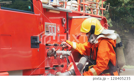 Fireman prepare equipment fighting extinguisher at fire engine truck. Firefighter fighting with smoke flame using fire hose, tube, chemical water foam spray at truck. Fireman wear hard hat protection Fireman prepare equipment fighting extinguisher at fire engine truck. Firefighter fighting with smoke flame using fire hose, tube, chemical water foam spray at truck. Fireman wear hard hat protection 128405235