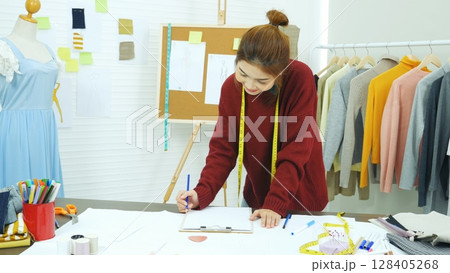 Entrepreneur fashion designer in textile business designing new retail clothing collection. Happy working woman seamstress, designer working on fabric sketches. Young designer fashion concept Entrepreneur fashion designer in textile business designing new retail clothing collection. Happy working woman seamstress, designer working on fabric sketches. Young designer fashion concept 128405268