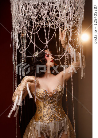 Circus show performer in vintage corset costume under chandelier on dark background Circus show performer in vintage corset costume under chandelier on dark background 128405287
