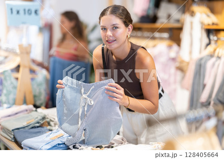 Young woman chooses trousers in clothing store Young woman chooses trousers in clothing store 128405664