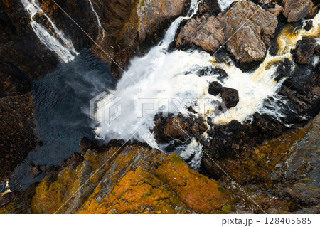 Powerful impact of Voringsfossen waterfall dramatically plunging into deep pool below. Swirling water contrasts sharply with dark rocks in Norway 128405685