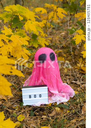 Halloween holiday concept. Handmade pink ghost with Lightbox BOO text made from bandages and glue in autumn forest background. Children's art project. DIY Halloween holiday concept. Handmade pink ghost with Lightbox BOO text made from bandages and glue in autumn forest background. Children's art project. DIY 128405781