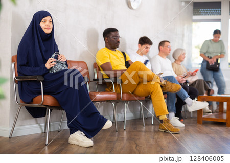 Girl in traditional veil, along with other people of different nationalities, is waiting for a specialist sitting on a chair in hall Girl in traditional veil, along with other people of different nationalities, is waiting for a specialist sitting on a chair in hall 128406005