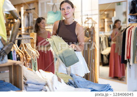 Two girls customer chooses jeans in store, and buyer carefully examines product. 128406045