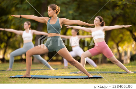 Happy women standing yoga pose and making full body stretching workout by female trainer in summer park 128406190