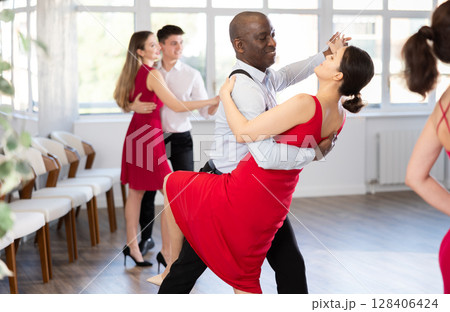 African American performing bachata with woman in red in dance studio 128406424