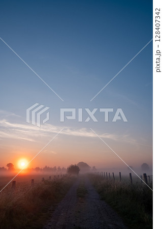 A Beautiful and Serene Sunrise Over the Misty Countryside Path Invites Exploration and Adventure A Beautiful and Serene Sunrise Over the Misty Countryside Path Invites Exploration and Adventure 128407342